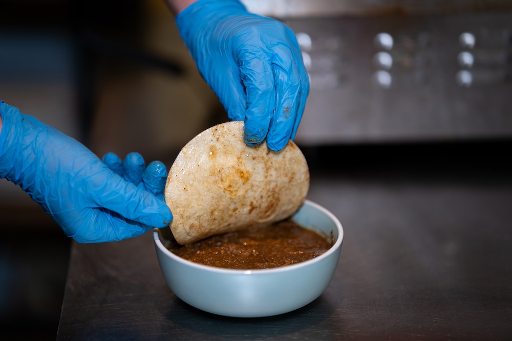 dipping tortilla in birria sauce before frying